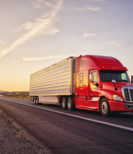 Large semi truck hauling freight on the open highway in the western USA under an evening sky.